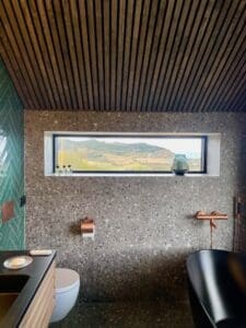 Panoramavindu med naturutsikt, terrazzo-flis, kobberarmaturer og frittstående svart badekar – baderomsrenovering Naustmarka, Malvik